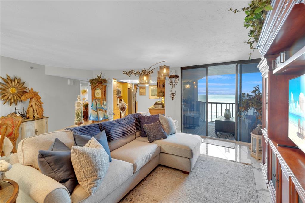 A bright living room features white furniture, a coffee table, and a balcony overlooking the ocean — 1600 GULF BOULEVARD UNIT 512, CLEARWATER BEACH, FL