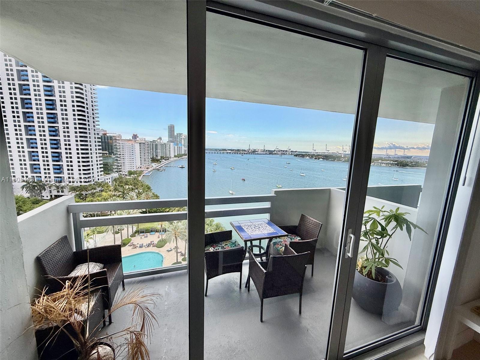 A balcony with outdoor furniture overlooks a bay, a swimming pool, and a city skyline — 1500 Bay Rd # 1534S, Miami Beach FL 33139, MIAMI BEACH, FL