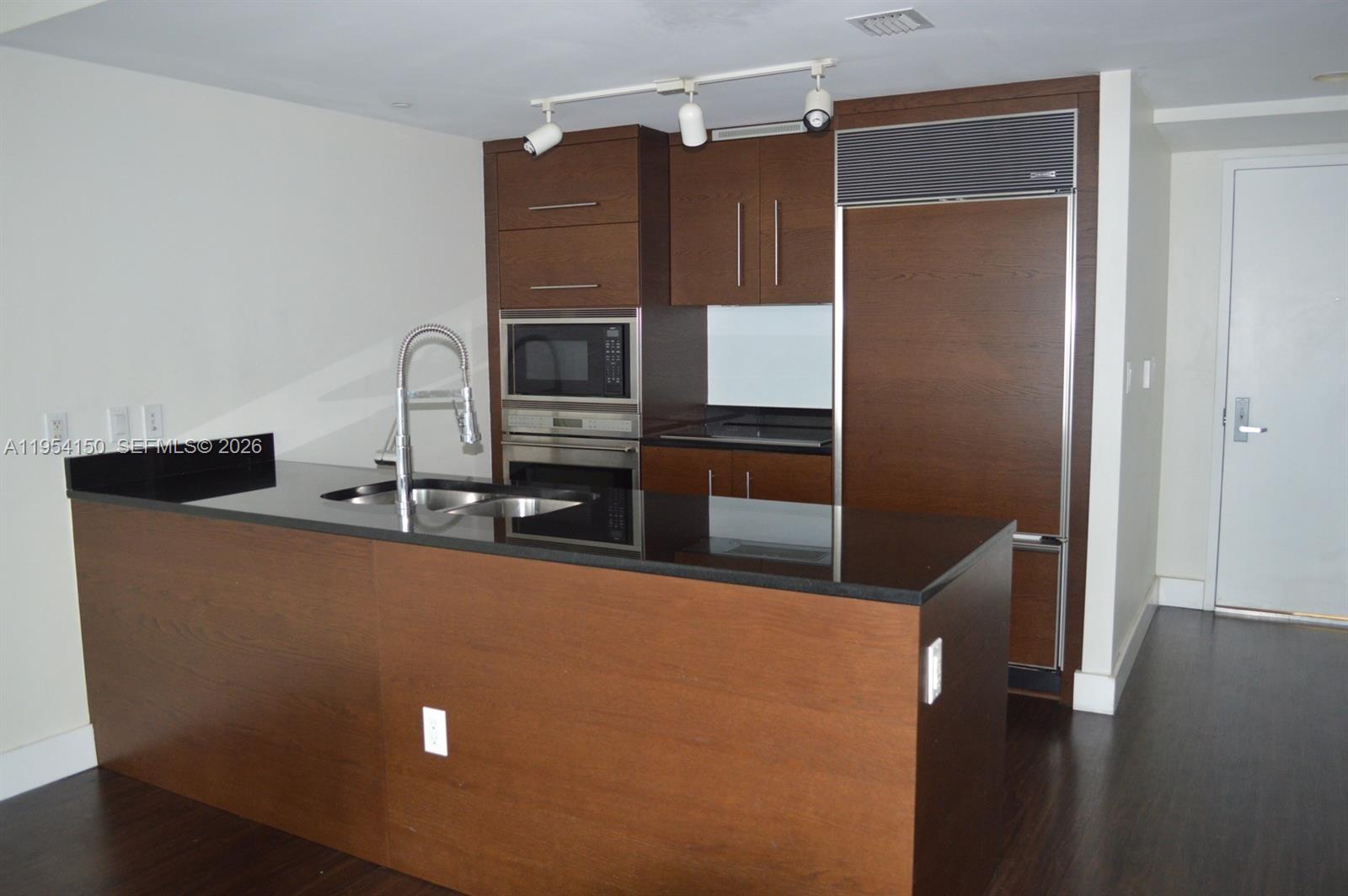 A kitchen features dark wood cabinetry, a black countertop island, and stainless steel appliances — 475 Brickell Ave # 1814, Miami FL 33131, MIAMI, FL