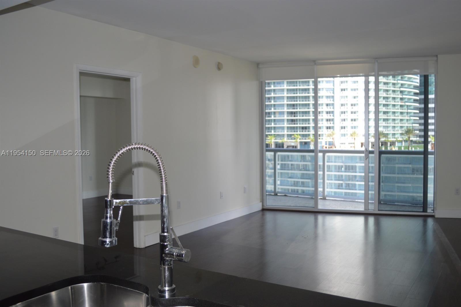 A kitchen sink with a chrome faucet overlooks an empty living area with floor-to-ceiling windows — 475 Brickell Ave # 1814, Miami FL 33131, MIAMI, FL