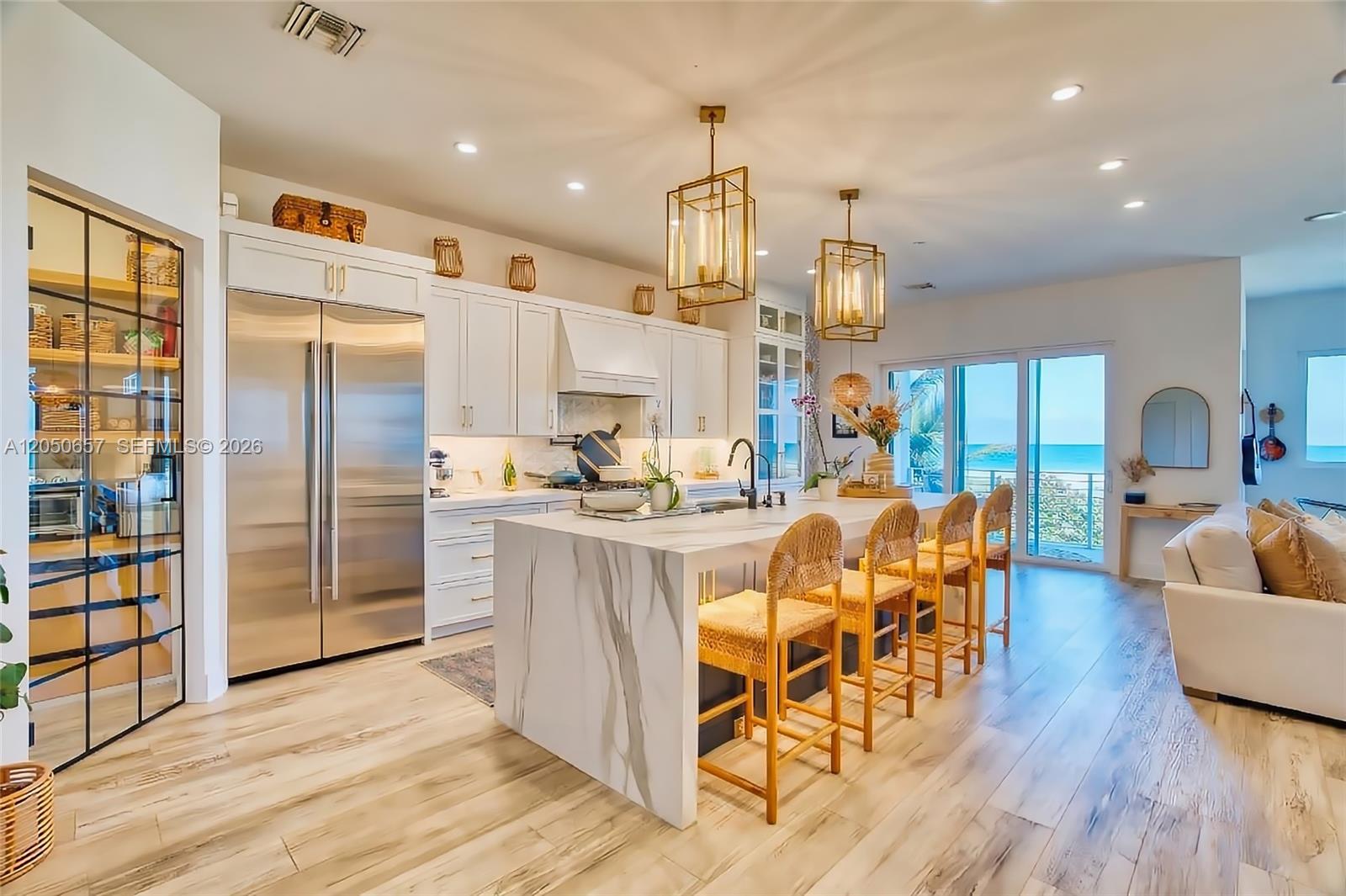 A modern kitchen features white cabinetry, a marble waterfall island, and a view of the ocean — 5120 Watersong Way, Fort Pierce FL 34949, FORT PIERCE, FL