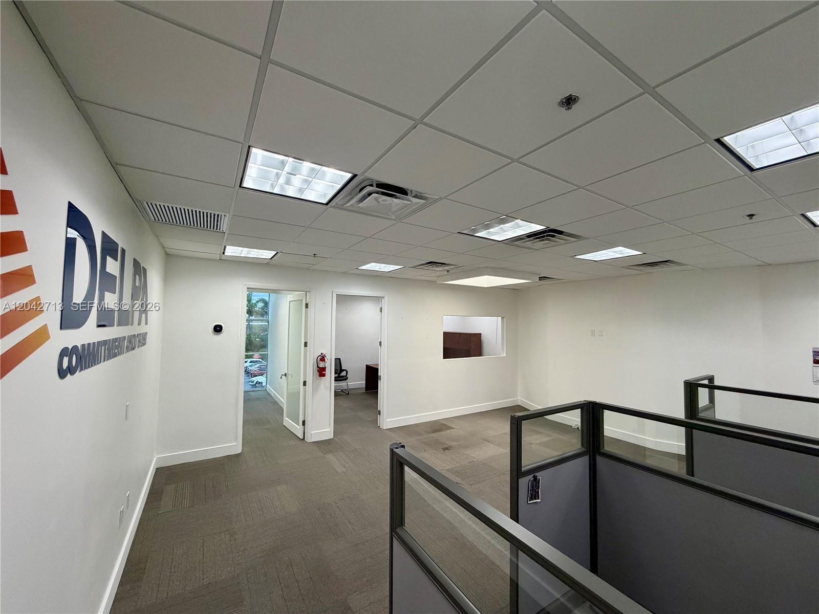 An office space features gray carpet, drop ceilings, cubicle partitions, and a white wall logo — 7500 NW 25th St # 205, Miami FL 33122, MIAMI, FL