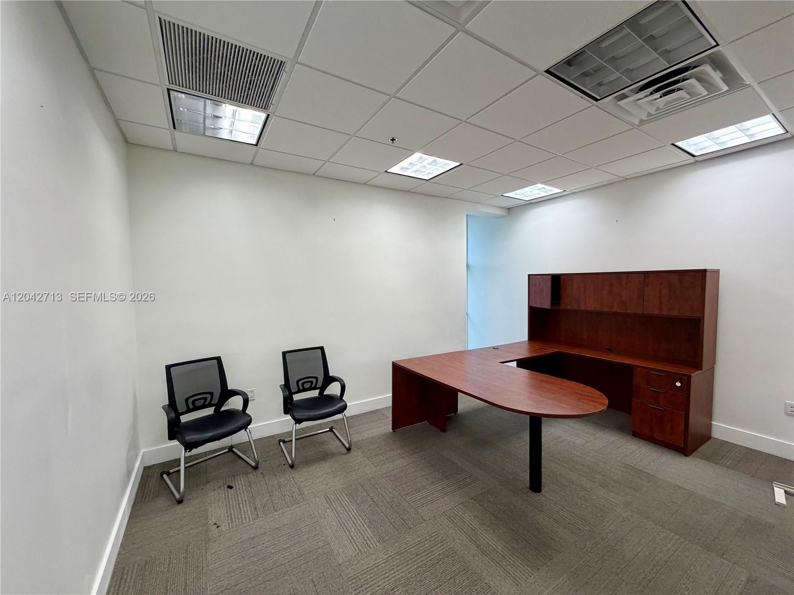 An office room features a wooden desk, two black chairs, and a drop ceiling — 7500 NW 25th St # 205, Miami FL 33122, MIAMI, FL