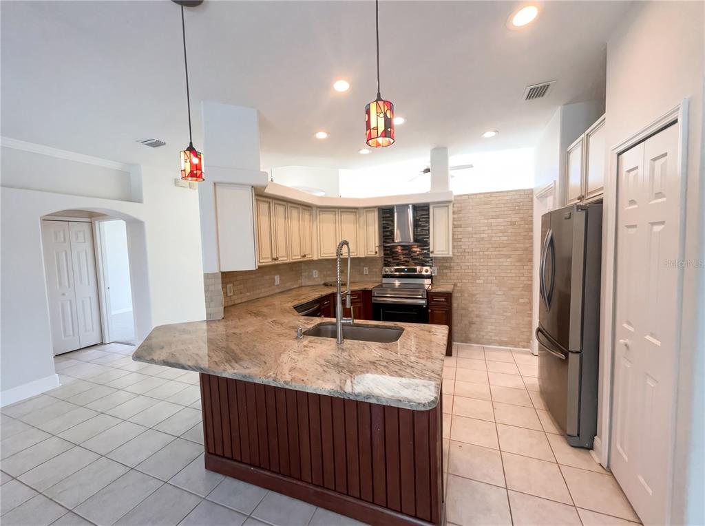 A kitchen features a granite-topped island, light-colored cabinets, stainless steel appliances, and tile flooring — 4241 SETTLERS COURT, ST CLOUD, FL