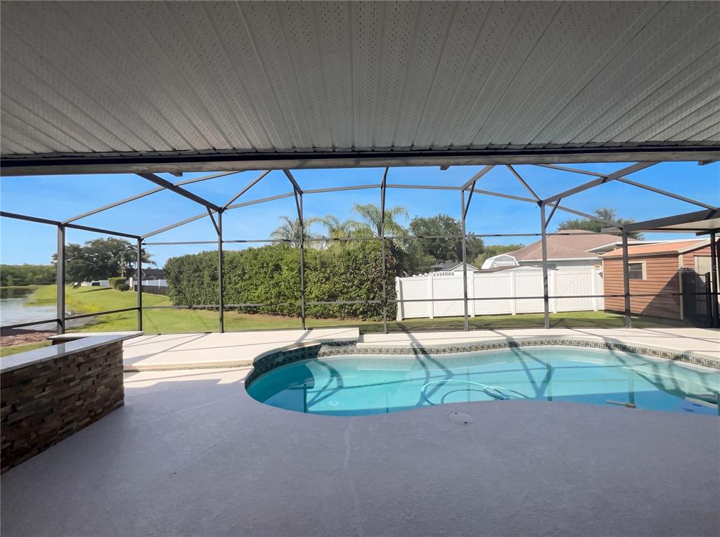 A covered patio features a swimming pool, a stone-faced bar, and a screened-in enclosure — 4241 SETTLERS COURT, ST CLOUD, FL