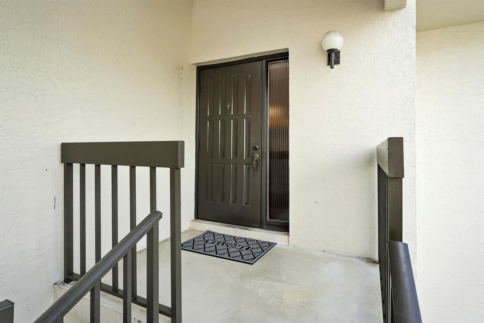 A dark brown front door with a sidelight sits on a concrete porch with railings — 402 Wingfoot Drive # B, Jupiter FL 33458, JUPITER, FL