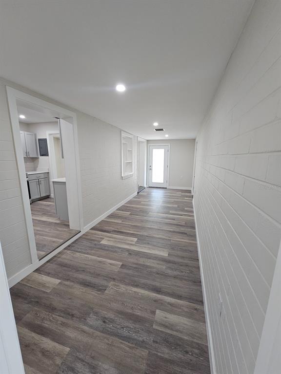 A long hallway with white painted brick walls and wood-look flooring leads to a door — 903 NW 33RD AVENUE, GAINESVILLE, FL