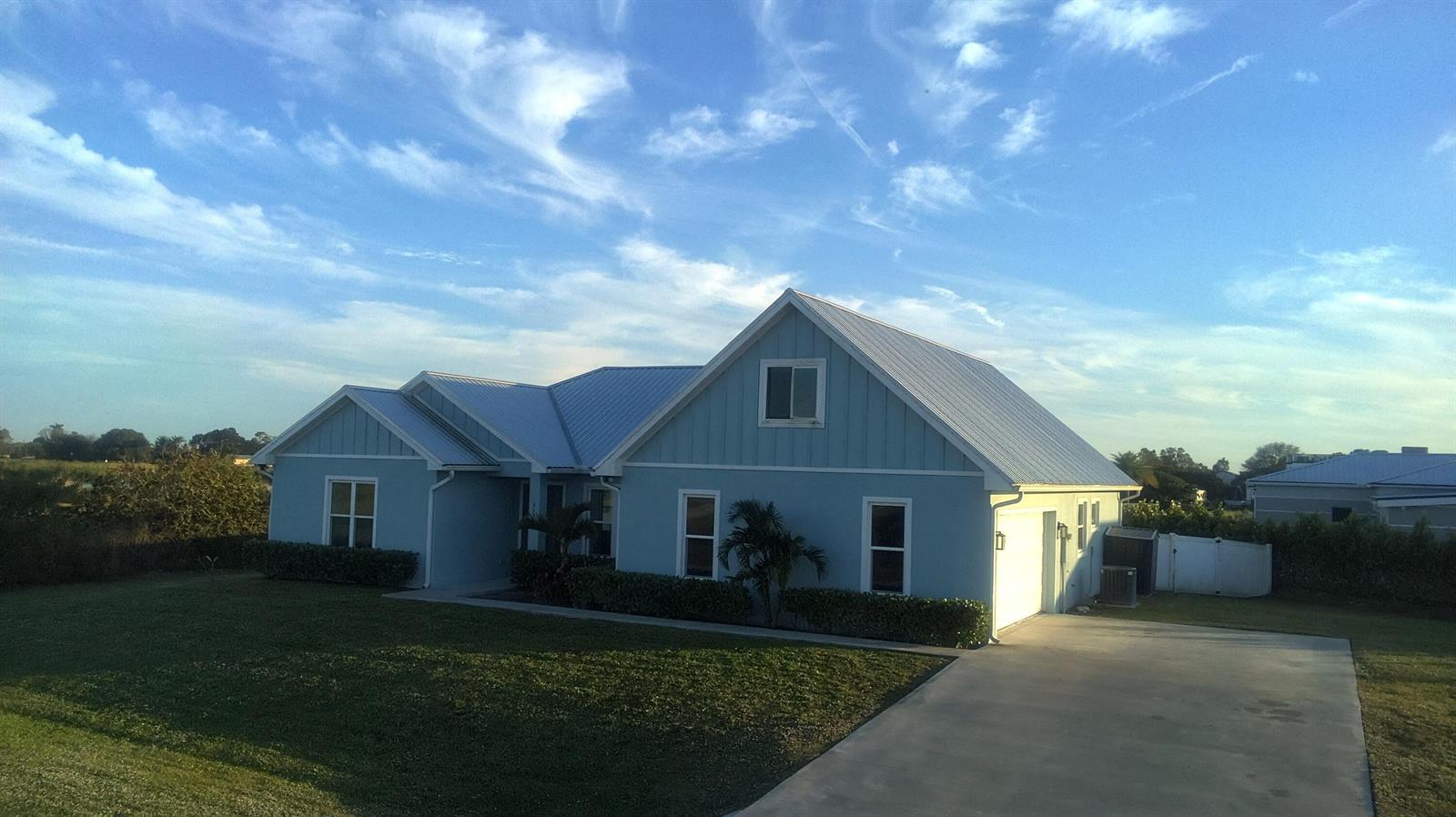 A light blue house with a metal roof and a concrete driveway under a blue sky — 3533 Sky Valley Lane, Clewiston FL 33440, CLEWISTON, FL