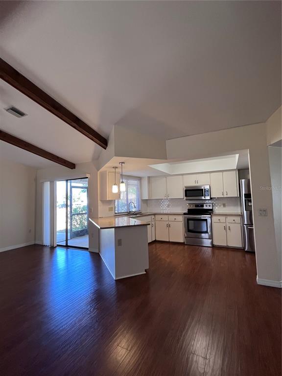 A kitchen with white cabinets and stainless steel appliances opens to a wood-floored living area — 5816 MONROE ROAD, VENICE, FL