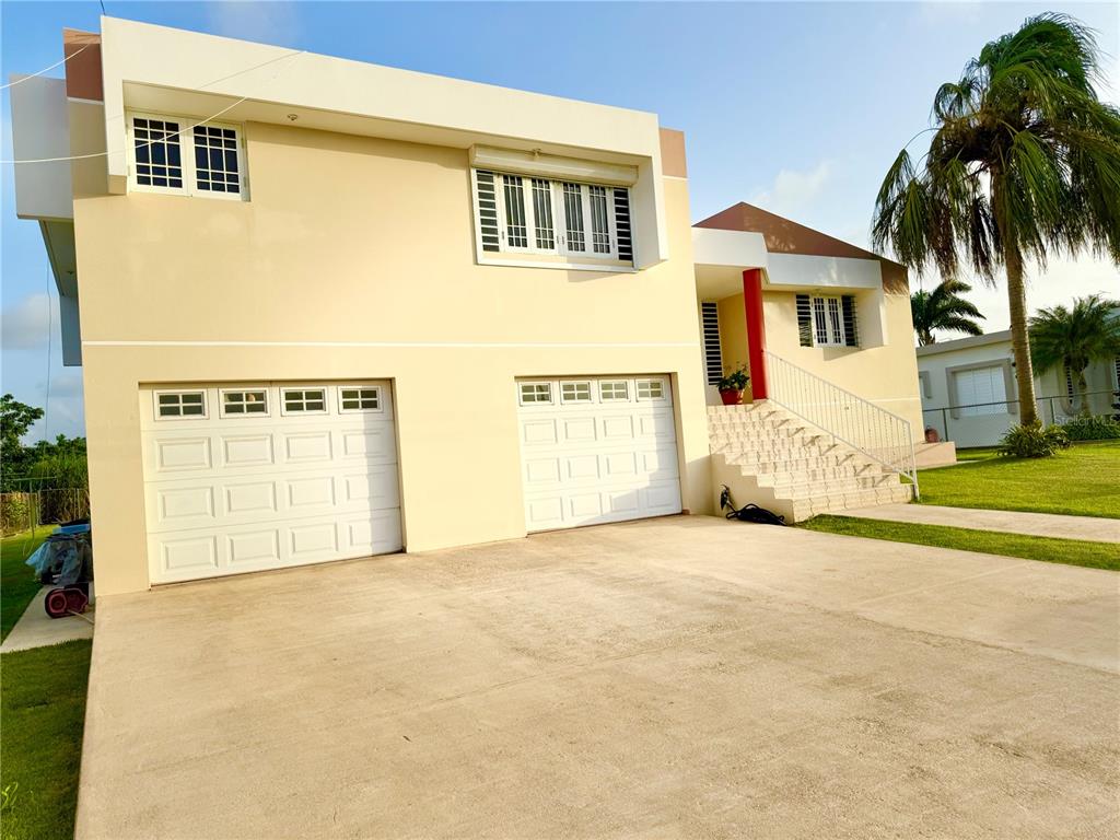 A two-story house with a beige exterior, a white garage, and a palm tree in front — Urb. La Romana 216 CALLE FRANCHESCO, QUEBRADILLAS, PR