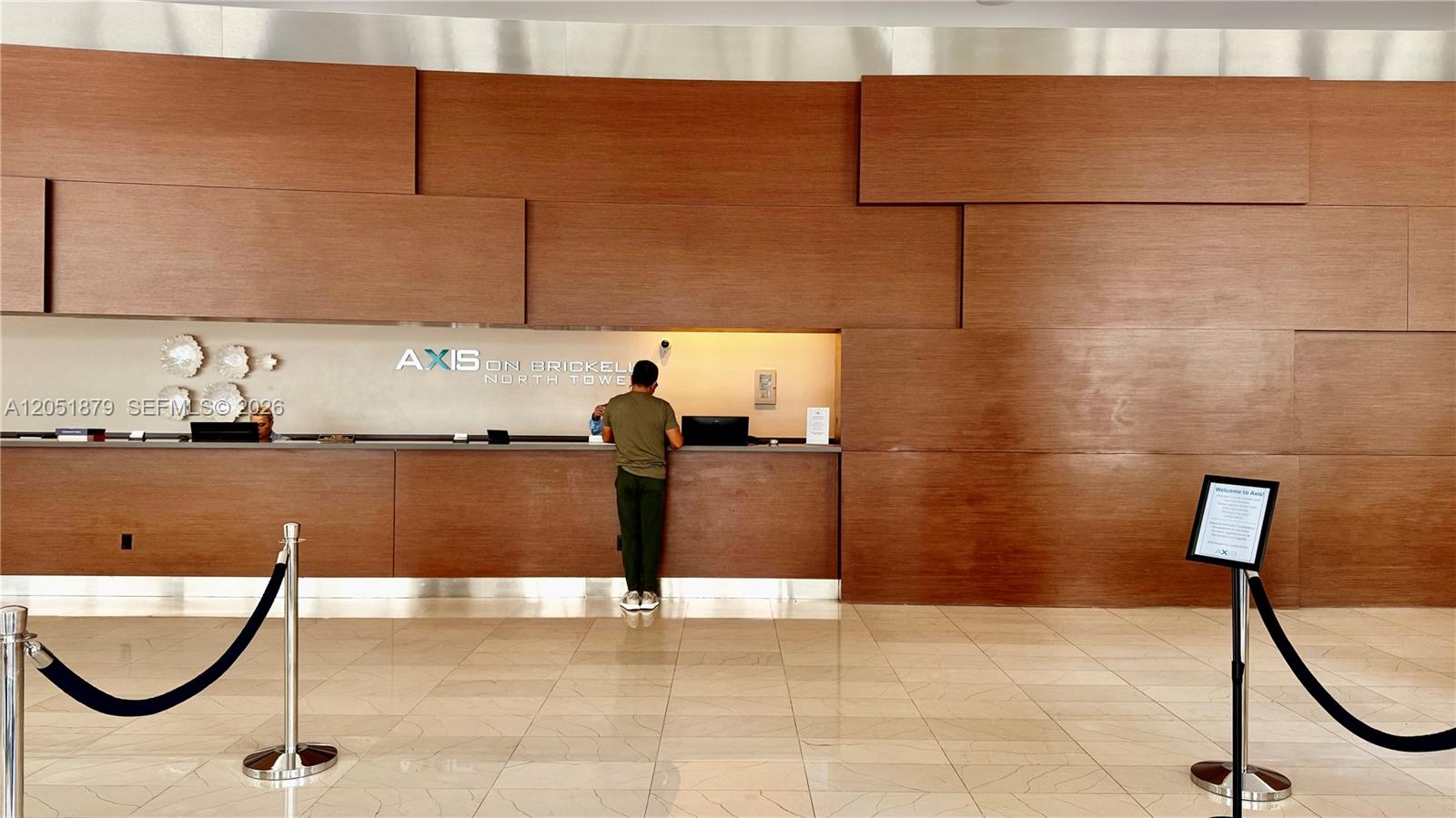 A person stands at a wood-paneled reception desk in a modern building lobby — 1111 SW 1st Ave, Miami FL 33130, MIAMI, FL