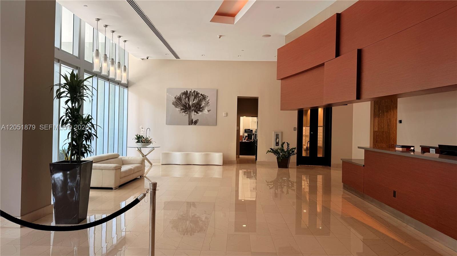 A modern lobby features a reception desk, floor-to-ceiling windows, and a white sofa — 1111 SW 1st Ave, Miami FL 33130, MIAMI, FL