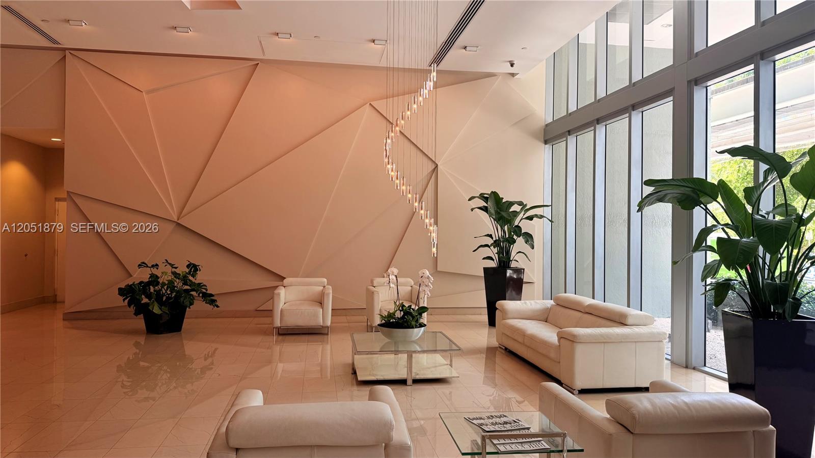 A modern lobby features a geometric accent wall, white leather furniture, and a hanging chandelier — 1111 SW 1st Ave, Miami FL 33130, MIAMI, FL