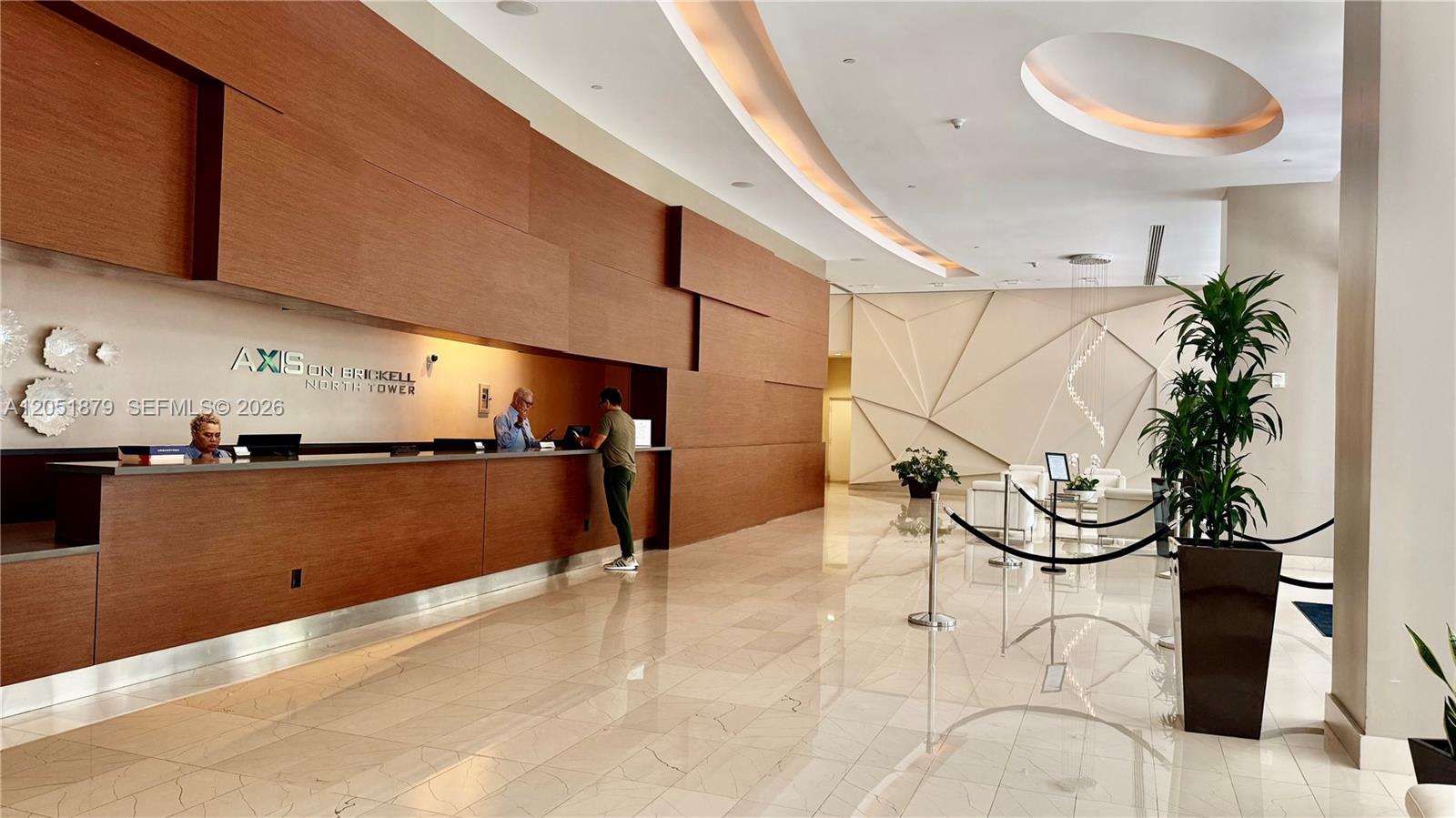 The lobby features a long wooden reception desk, marble flooring, and a decorative wall installation — 1111 SW 1st Ave, Miami FL 33130, MIAMI, FL