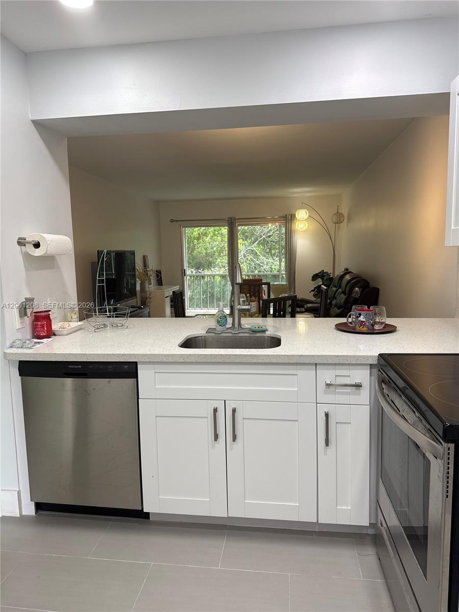 A kitchen with white cabinets, stainless steel appliances, and a pass-through window to the living area — 1102 Bahama Bnd # D2, Coconut Creek FL 33066, COCONUT CREEK, FL