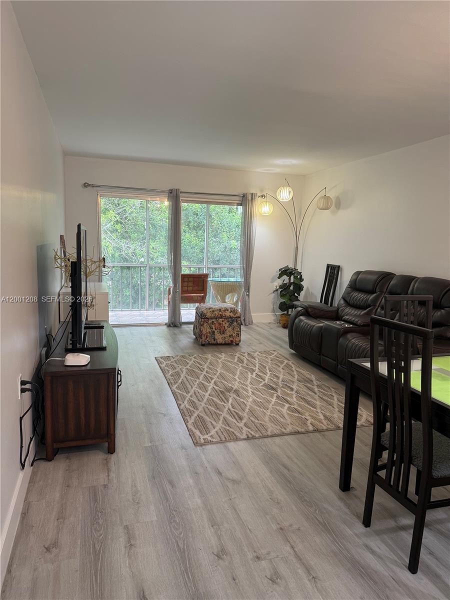 A living room features light wood-look flooring, a dark leather sofa, and a sliding glass door — 1102 Bahama Bnd # D2, Coconut Creek FL 33066, COCONUT CREEK, FL