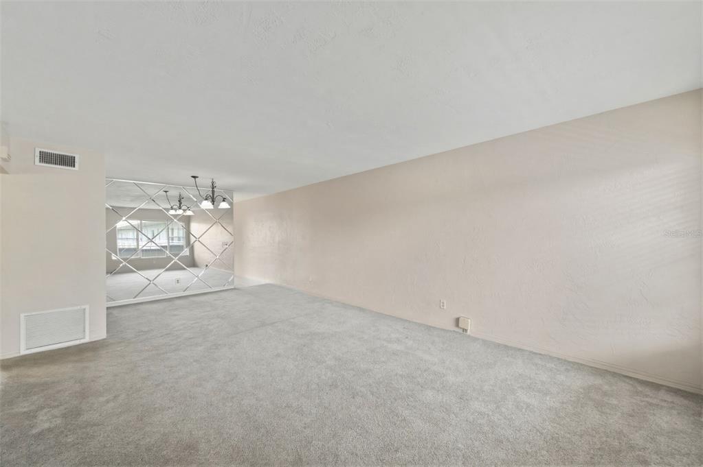 An empty room features gray carpeting, a large mirrored wall, and a plain beige wall — 2462 BRAZILIA DRIVE UNIT 70, CLEARWATER, FL
