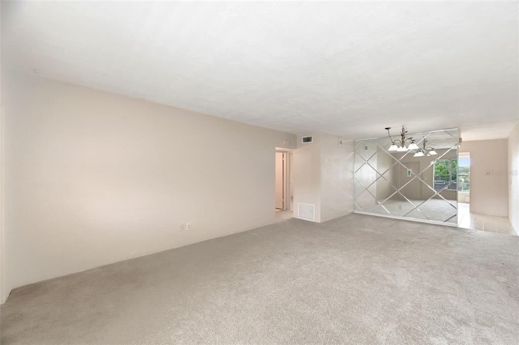 A living room features beige carpeting, plain walls, and a large diamond-patterned mirrored accent wall — 2462 BRAZILIA DRIVE UNIT 70, CLEARWATER, FL