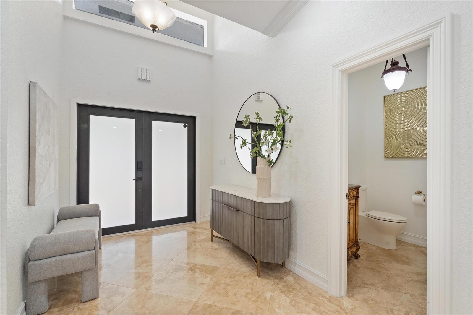 A bright entryway features a gray console table, a round mirror, and a tiled floor — 10076 El Caballo Court, Delray Beach FL 33446, DELRAY BEACH, FL
