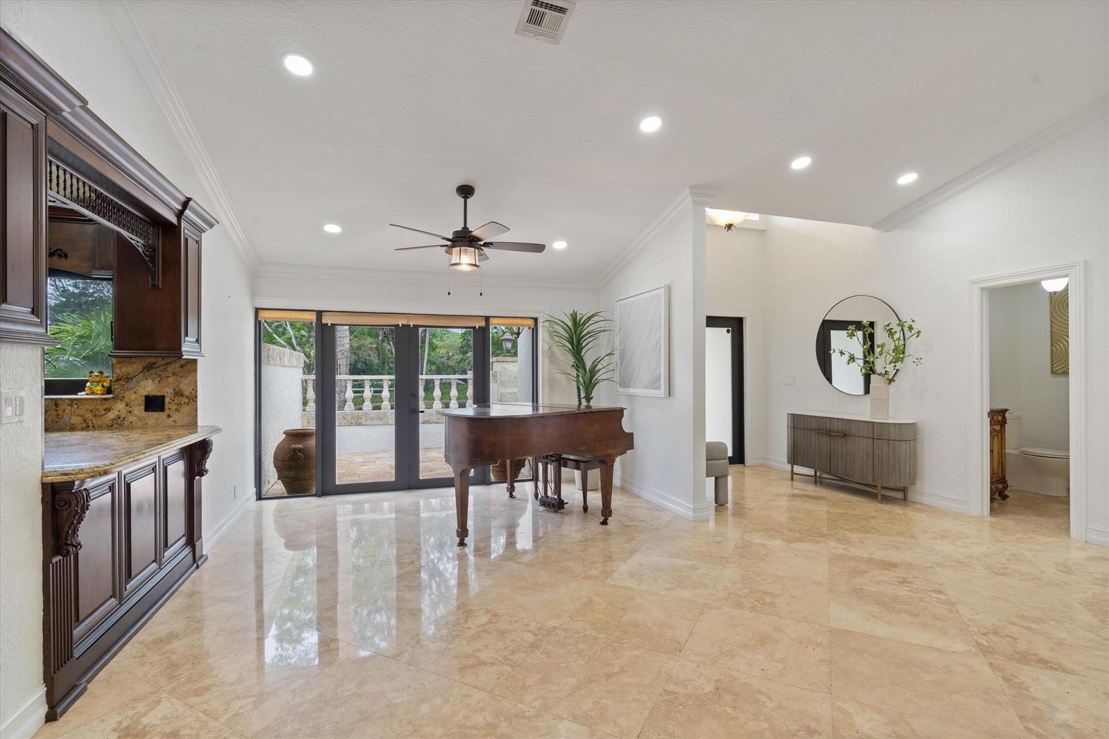 A room with a grand piano, dark wood cabinetry, and tile flooring leads to a patio — 10076 El Caballo Court, Delray Beach FL 33446, DELRAY BEACH, FL