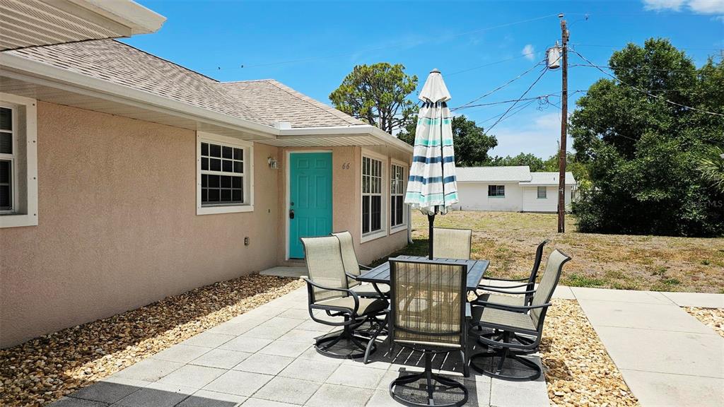 A patio with a dining set and umbrella sits outside a house with a teal door — 66 N MCCALL, ENGLEWOOD, FL