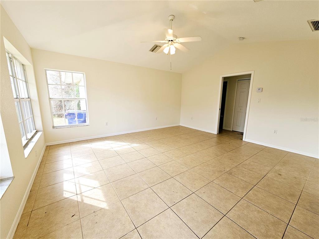 An empty living room features beige tile flooring, a vaulted ceiling with a fan, and windows — 66 N MCCALL, ENGLEWOOD, FL