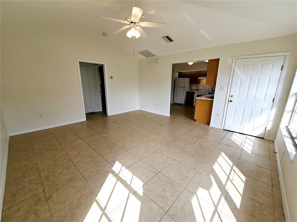 A living room with beige tile flooring, a ceiling fan, and an open kitchen doorway — 66 N MCCALL, ENGLEWOOD, FL