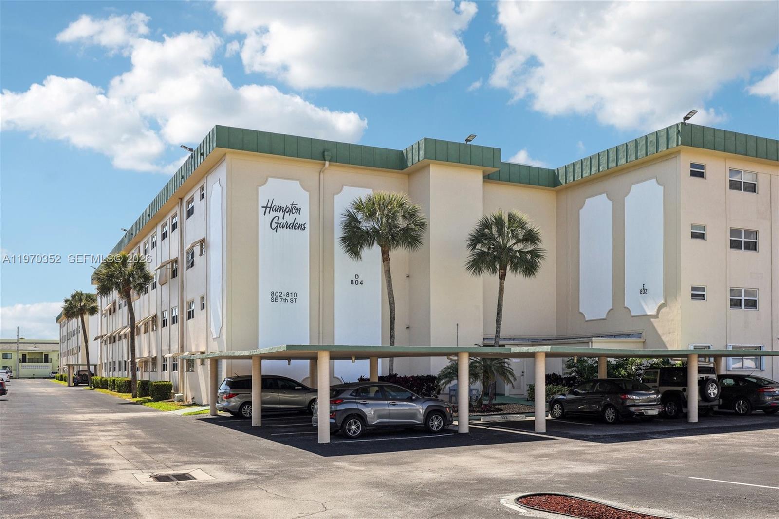 The exterior of a multi-story apartment building features a covered parking area and palm trees — 804 SE 7th St # 402, Deerfield Beach FL 33441, DEERFIELD BEACH, FL