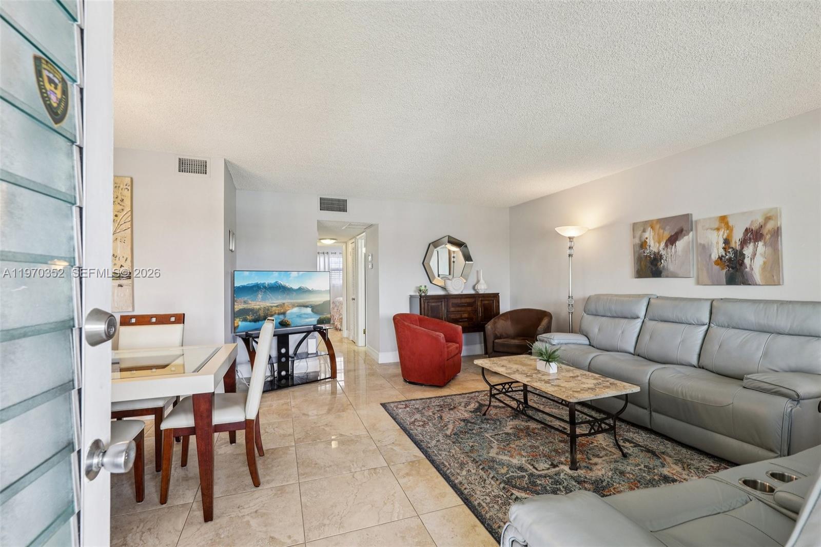 A living room with tile floors, a gray sofa, a red chair, and a dining area — 804 SE 7th St # 402, Deerfield Beach FL 33441, DEERFIELD BEACH, FL