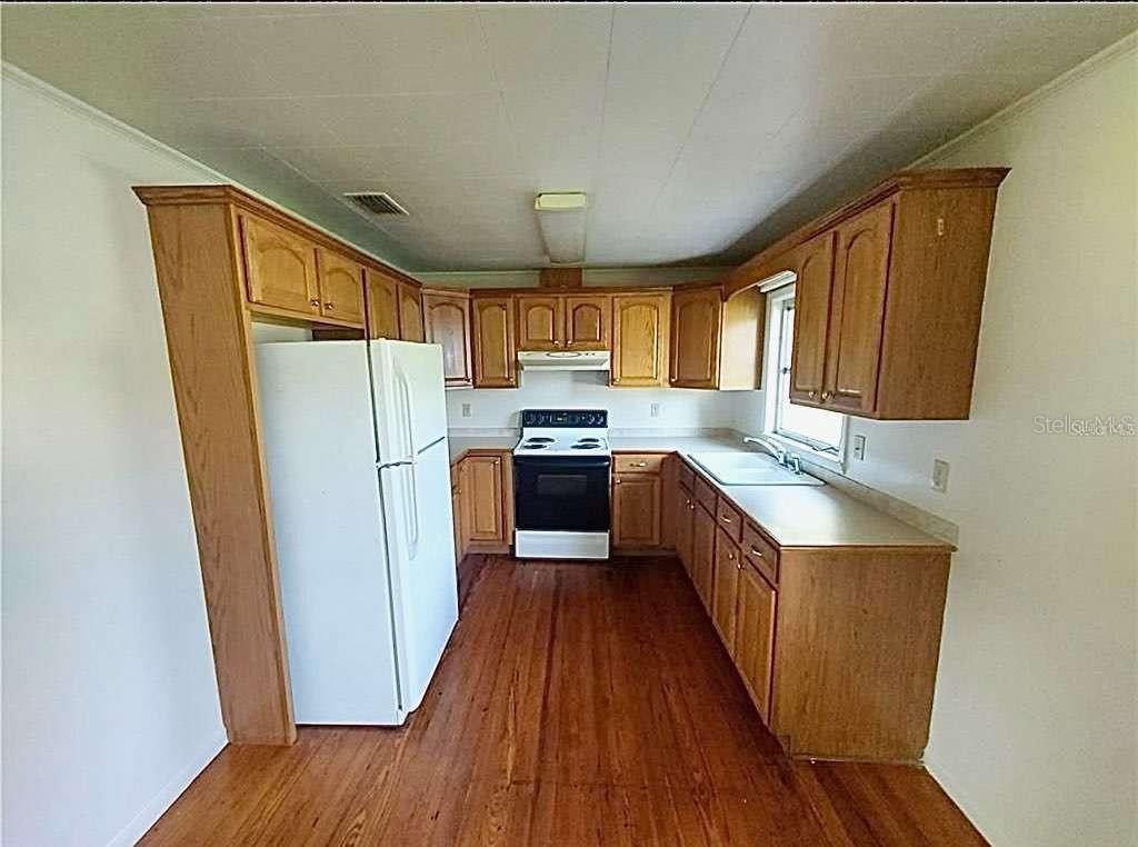A kitchen features wood cabinets, white appliances, laminate countertops, and hardwood flooring — 1551 NE 29TH STREET, OCALA, FL