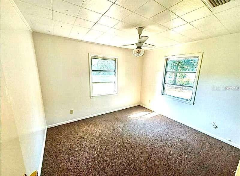 An empty bedroom features brown carpet, white walls, a ceiling fan, and two windows — 1551 NE 29TH STREET, OCALA, FL