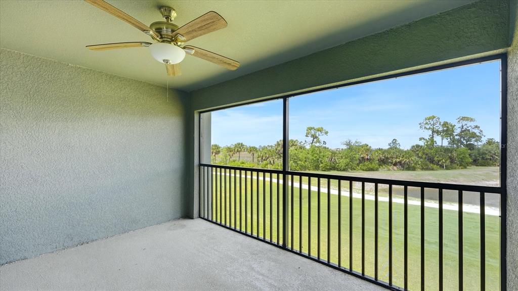 A covered balcony features a ceiling fan, textured walls, and a black railing overlooking greenery — 17475 OPAL SAND DRIVE UNIT 208, VENICE, FL