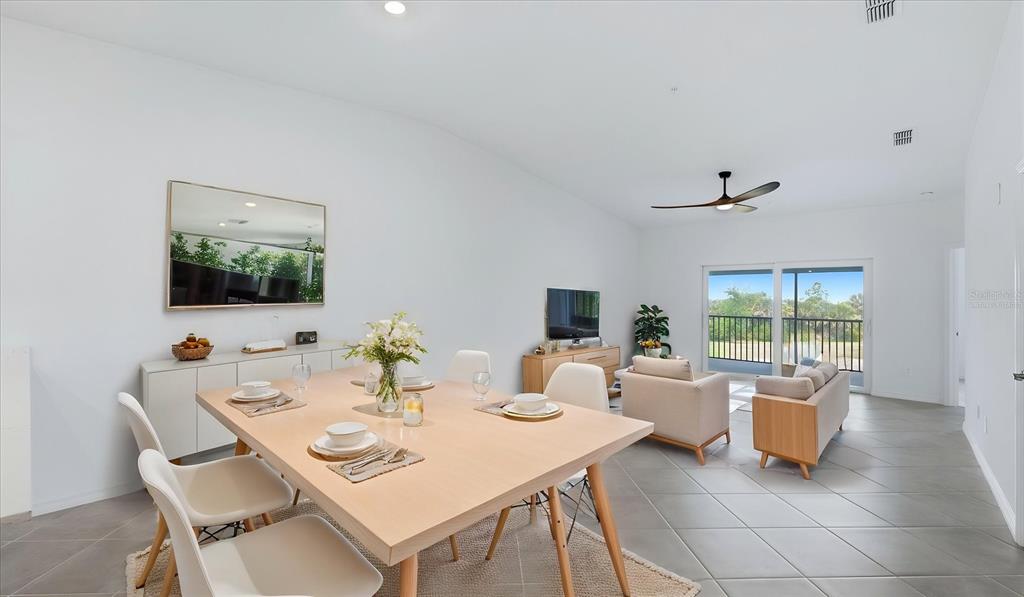 A dining area with a light wood table opens into a living room with tile floors — 17475 OPAL SAND DRIVE UNIT 208, VENICE, FL