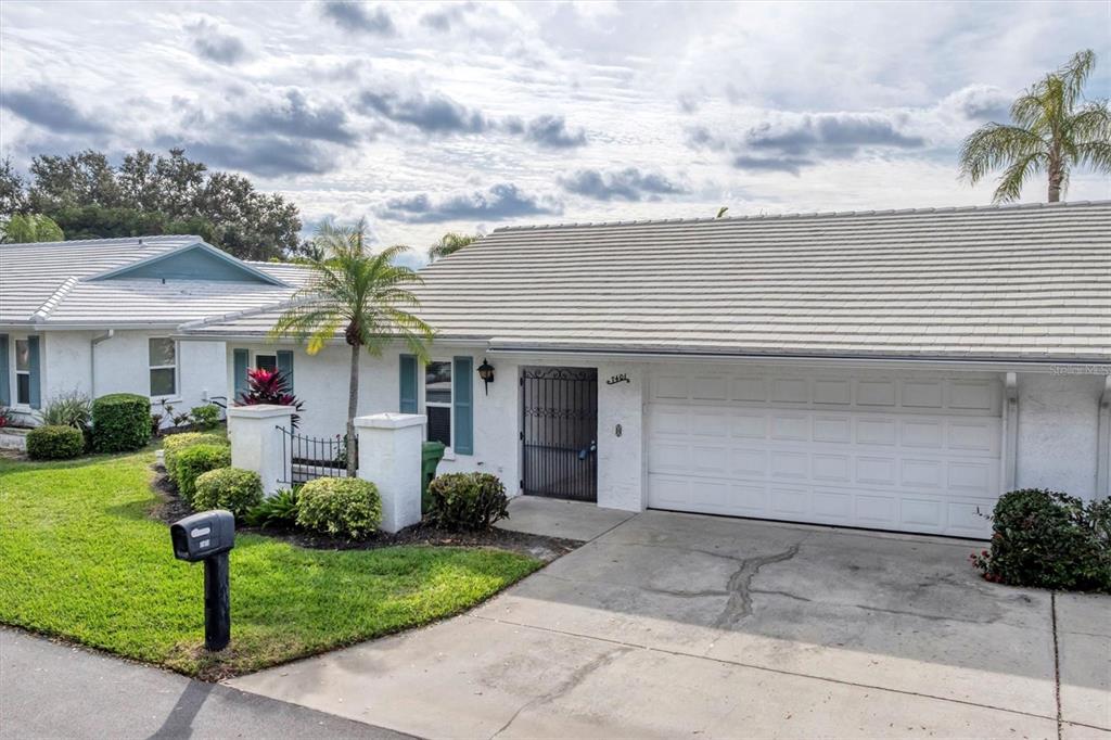A white single-story house with a two-car garage, tile roof, and a gated courtyard entrance — 7401 7TH AVENUE W UNIT 5807, BRADENTON, FL