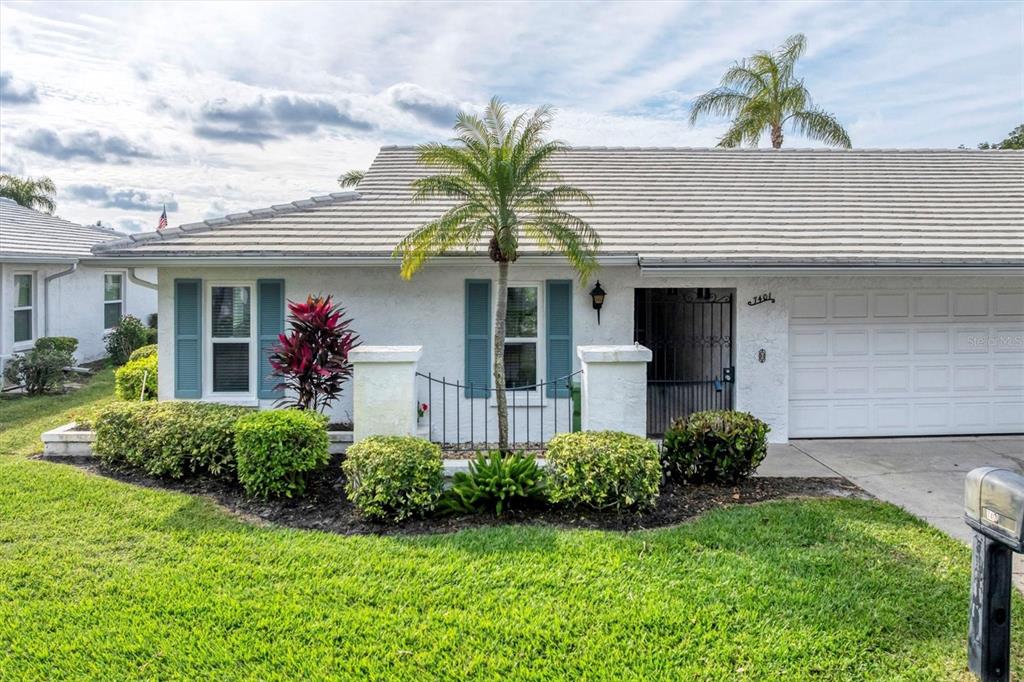 A single-story white house with a tile roof, blue shutters, and a front courtyard — 7401 7TH AVENUE W UNIT 5807, BRADENTON, FL
