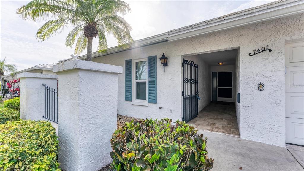 A white stucco house exterior features a palm tree, blue shutters, and a gated entryway — 7401 7TH AVENUE W UNIT 5807, BRADENTON, FL