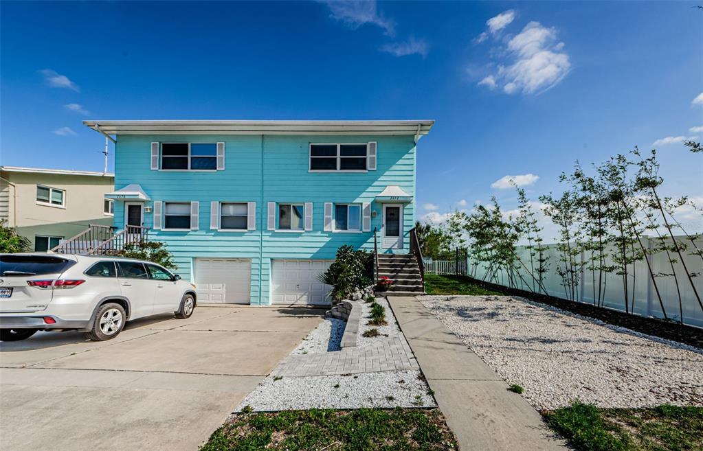 A two-story, light blue duplex features a concrete driveway, two garage doors, and exterior stairs — 2672 ST JOSEPHS DRIVE, DUNEDIN, FL