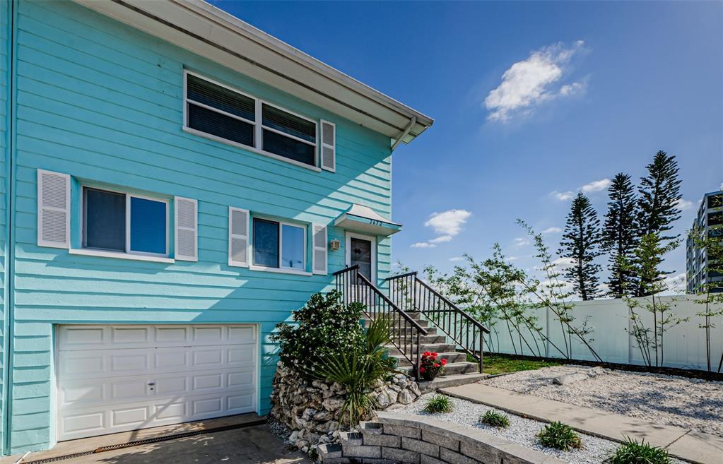 A two-story light blue house with a garage, stairs to the entrance, and landscaping — 2672 ST JOSEPHS DRIVE, DUNEDIN, FL