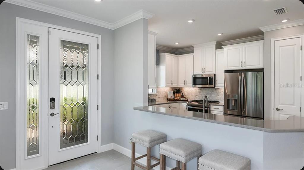 A kitchen with white cabinets and stainless steel appliances overlooks a breakfast bar and entryway — 3130 TORTA COURT, BRADENTON, FL