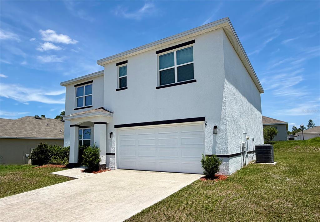 A two-story white stucco house features a two-car garage and a concrete driveway — 39 HICKORY COURSE WAY, OCALA, FL