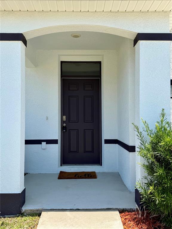 A dark front door with a transom window is set within a covered porch entrance — 39 HICKORY COURSE WAY, OCALA, FL