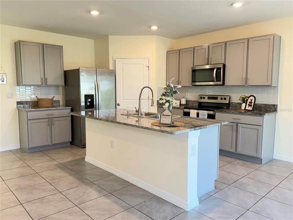 A kitchen with gray cabinets, granite countertops, stainless steel appliances, and a central island — 39 HICKORY COURSE WAY, OCALA, FL