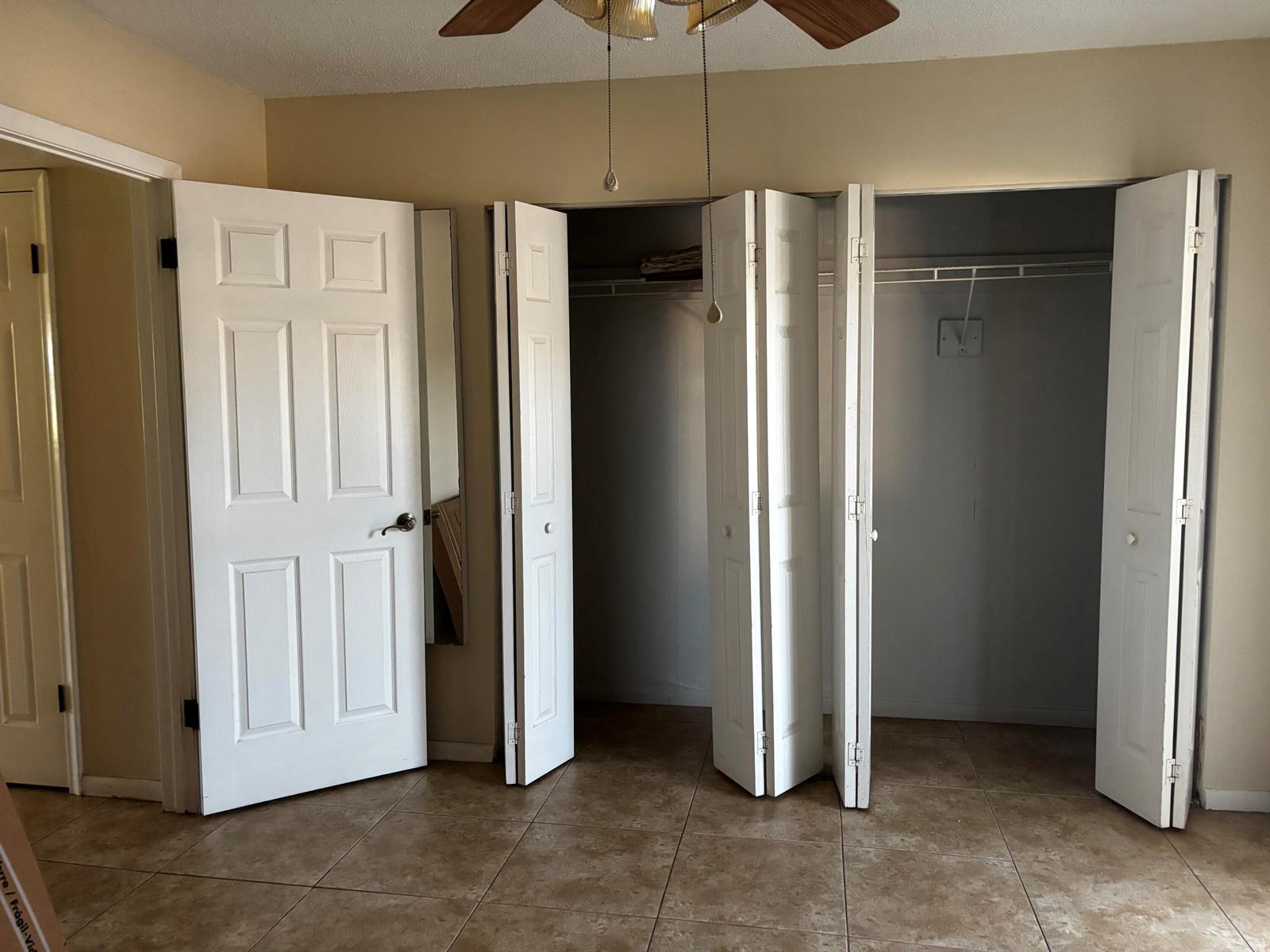 A bedroom features beige walls, tile flooring, a ceiling fan, and open bi-fold closet doors — 284 Windsor M, West Palm Beach FL 33417, WEST PALM BEACH, FL