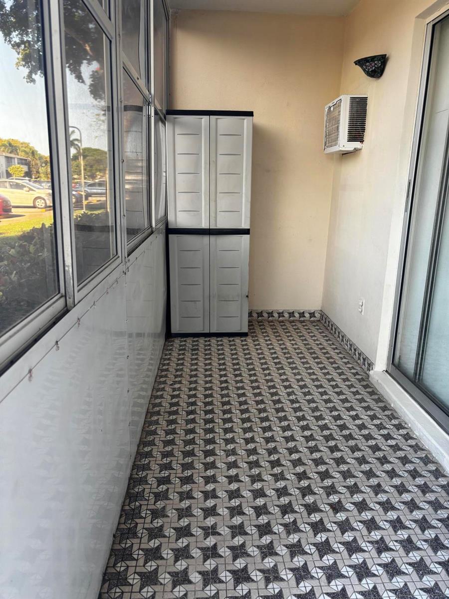 A tiled balcony features a tall plastic storage cabinet and a wall-mounted air conditioning unit — 284 Windsor M, West Palm Beach FL 33417, WEST PALM BEACH, FL
