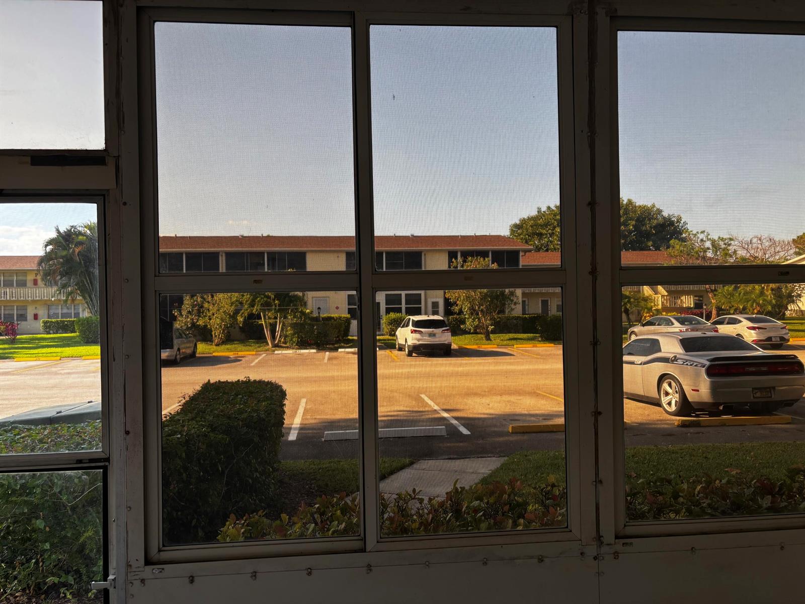 View of a parking lot and apartment buildings through a screened-in porch window — 284 Windsor M, West Palm Beach FL 33417, WEST PALM BEACH, FL