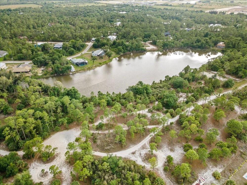 An aerial view shows a lake surrounded by trees, sandy paths, and several residential houses — 27205 MONTE CRISTO BOULEVARD, PUNTA GORDA, FL