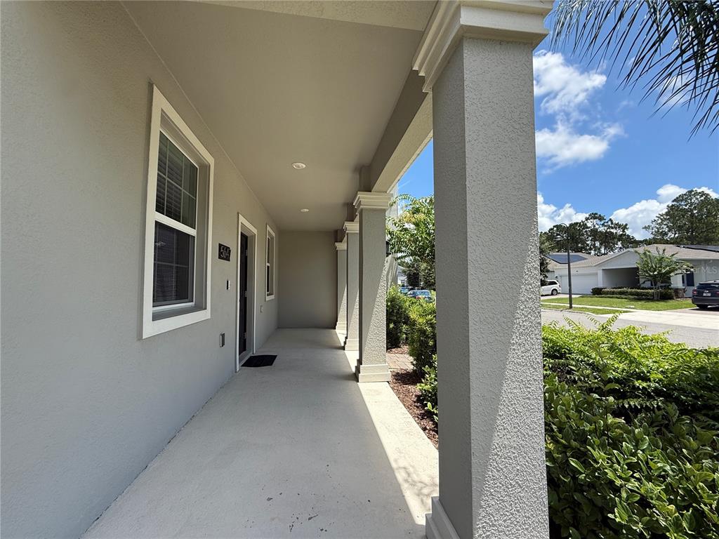 A covered front porch features gray stucco walls, square columns, and a concrete floor — 5647 QUIET PALM LOOP, ST CLOUD, FL