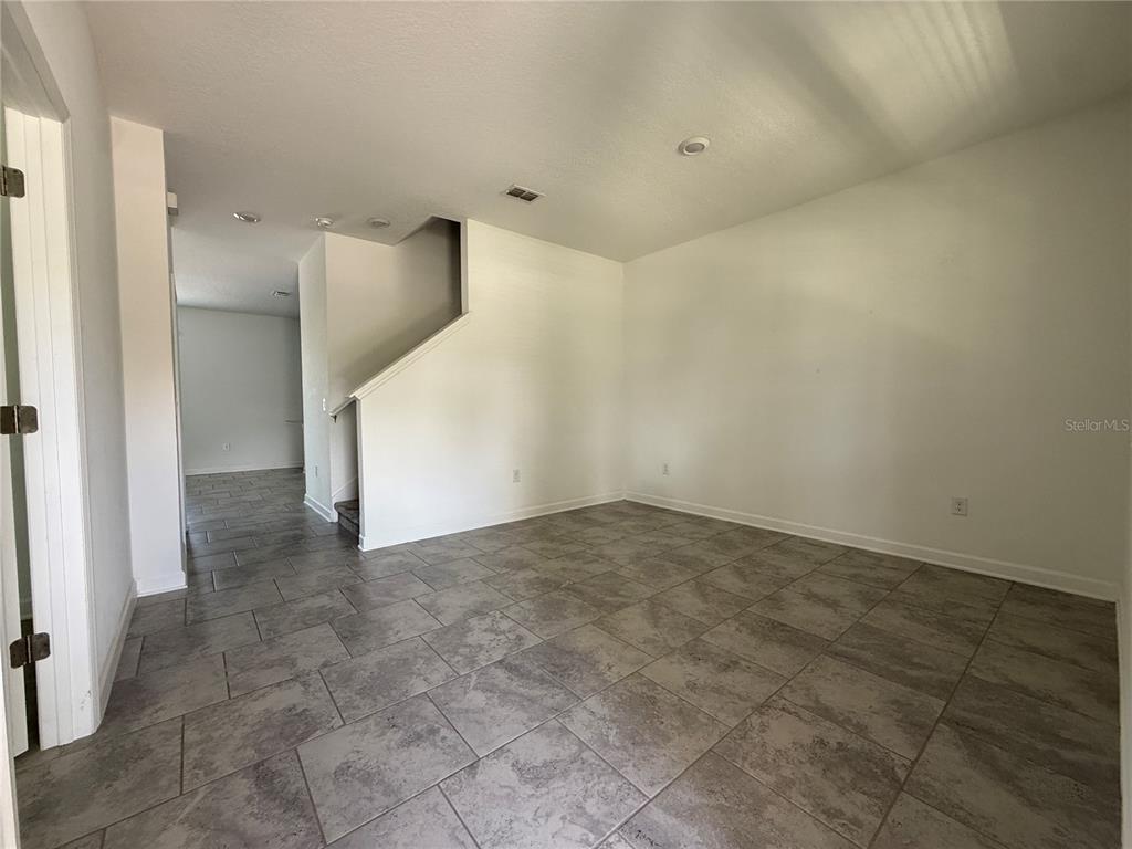 An empty room with gray tile flooring, white walls, and a staircase in the background — 5647 QUIET PALM LOOP, ST CLOUD, FL