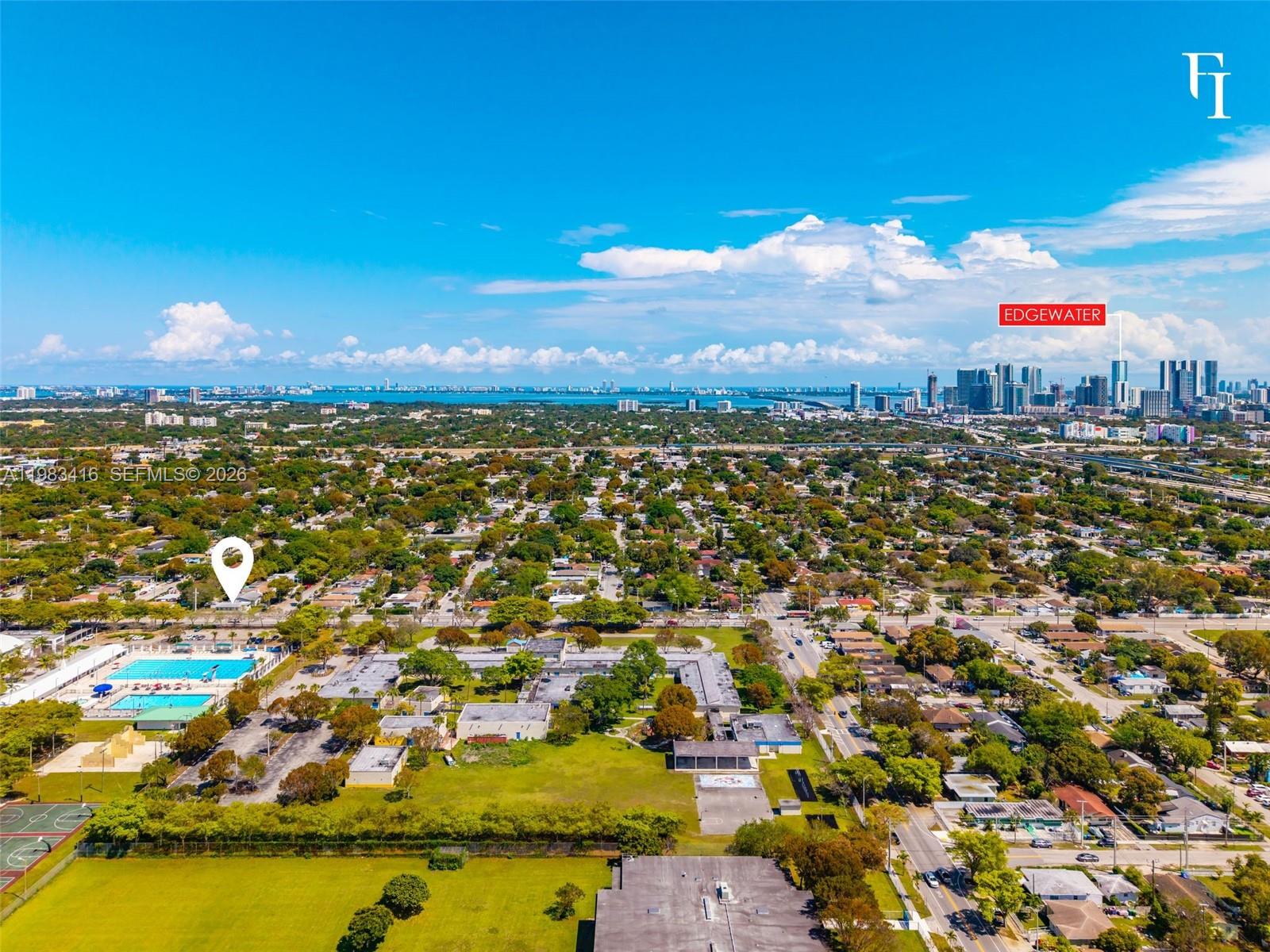 This aerial view shows a suburban neighborhood with a swimming pool and distant city skyline — 1195 NW 48th St, Miami FL 33127, MIAMI, FL