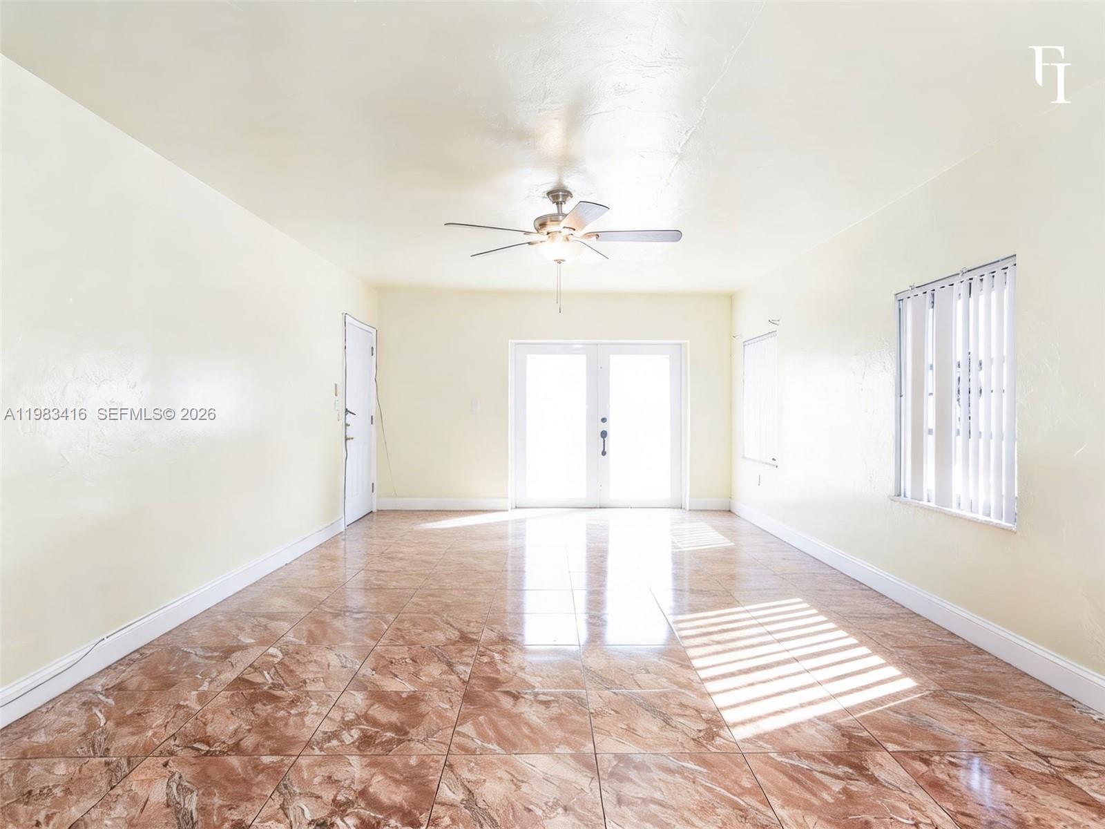 An empty room features light yellow walls, brown marble-style tile flooring, and a ceiling fan — 1195 NW 48th St, Miami FL 33127, MIAMI, FL